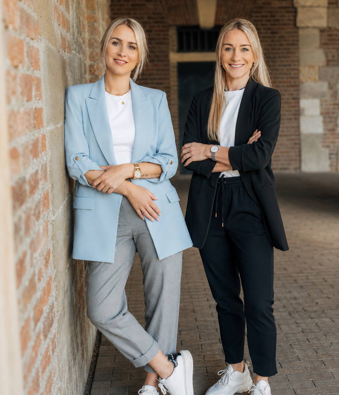 Anna Heuvens und Lena Altmann, die beiden Gründerinnen von AL Werbekonzept, stehen nebeneinander an einer Backsteinwand.
